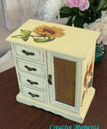 Dixie Belle Paint Lemonade Chalk Mineral Paint is the perfect paint for any DIY project!
project!
Jewelry box painted with black hardware and the Sunflowers Transfer is seen on the top of the piece and on the side panel as well. Staged besides a glass vase of white and pink flowers on a brown wood platform.