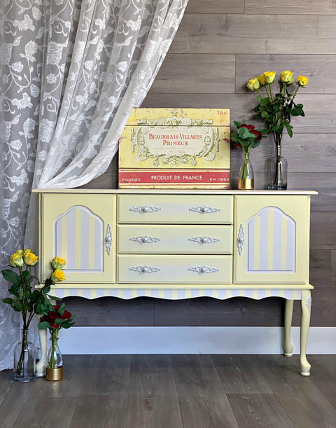 Dixie Belle Paint Lemonade Chalk Mineral Paint is the perfect paint for any DIY project!
Credenza painted in Lemonade Chalk Mineral Paint with gray stripes on the door panels and trim. along with white hardware, staged with glass bottles and yellow/red roses inside them.