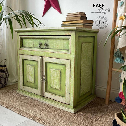 Dixie Belle Paint Limeade Chalk Mineral Paint is the perfect paint for any DIY project!
A Cabinet painted with a mix of Limeade and Evergreen Chalk Mineral Paint, there are off white areas around the edges of the door and the drawer. Staged with a stack of books on top, as well as a ladder with multiple colors hanging on it to the right side of the piece.