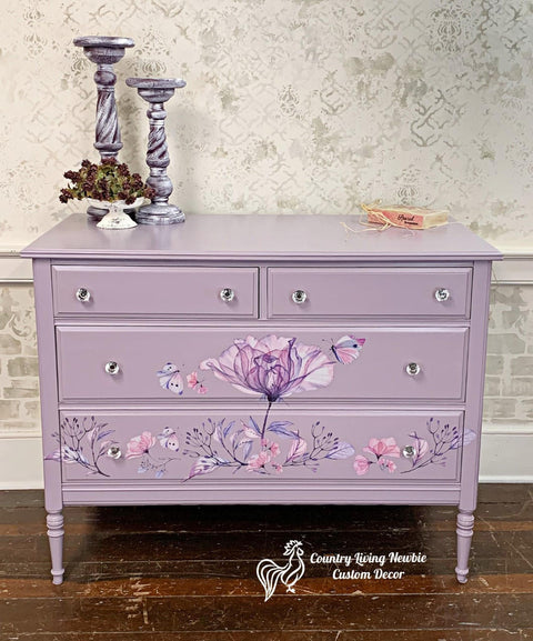 Dixie Belle Paint Lucky Lavender Chalk Mineral Paint is the perfect paint for any DIY project!
Dresser painted in Lucky Lavender CMP with Translucent Garden - Transfer across the the long drawers with crystal hardware. Staged on wooden floor and two lavender distressed candle holders on top.