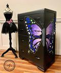Dixie Belle Paint Lucky Lavender Chalk Mineral Paint is the perfect paint for any DIY project!
Black dresser with a hand painted butterfly split between the front and side of dresser. Lucky Lavender Chalk Mineral Paint is seen on the inside of the wing to the butterfly. Staged with a body mannequin with a black tutu dress and pink  butterfly.