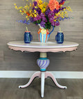 Dixie Belle Paint Lucky Lavender Chalk Mineral Paint is the perfect paint for any DIY project!
Table painted in white and pink with Lucky Lavender Chalk Mineral Paint  used as an accent color along the base.. Staged with a blue,yellow,and orange pitcher with multicolored flowers and two blue mason jar cups  on each side.