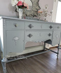 Dixie Belle Paint Manatee Gray Chalk Mineral Paint is the perfect paint for any DIY project! Light Gray Chalk Painted desk with Silver Accents. Staged with a candle stick holder and vase with flowers.