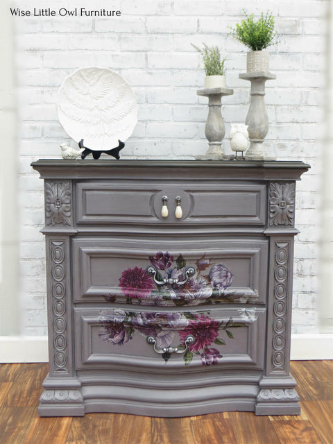 Dixie Belle Paint Mason Dixon Gray Chalk Mineral Paint is the perfect paint for any DIY project! Dark Gray Chalk painted End table with a floral rub on transfer. Staged with two candle stick holders with small potted plants and a plate holder with a white shell shaped plate, along with two small bird figures.