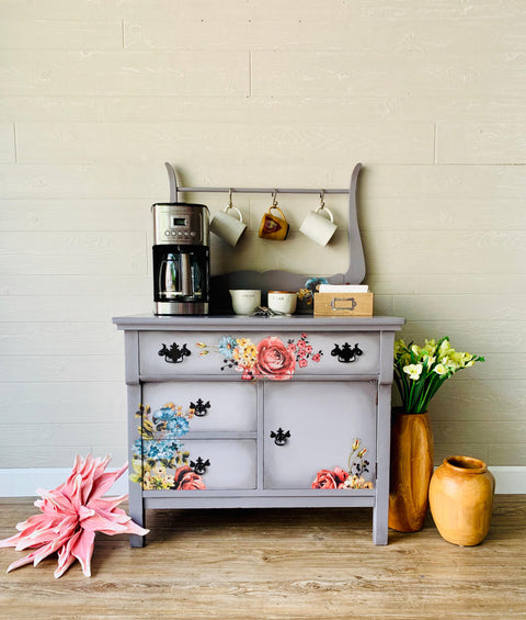 Dixie Belle Paint Mason Dixon Gray Chalk Mineral Paint is the perfect paint for any DIY project! Light Gray Chalk painted Vintage dresser turned into coffee bar with floral rub on transfers. Staged with cups, a coffee maker, cream and sugar and some napkins. Also has two wooden vases with plants in them besides it.