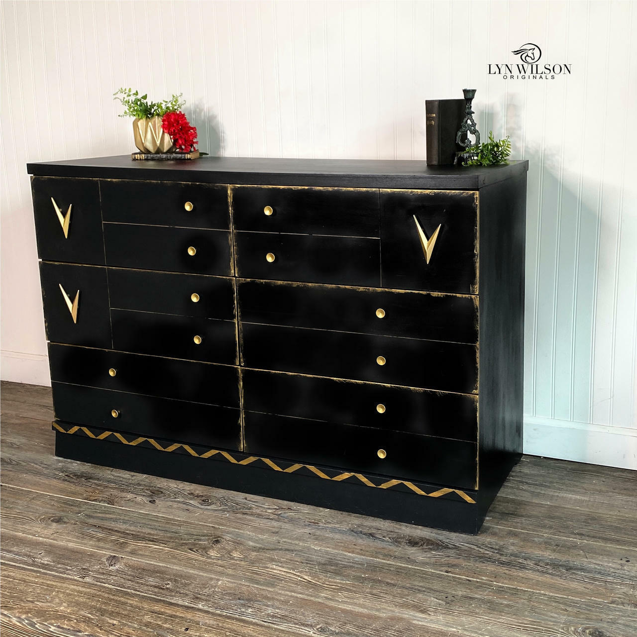 Dixie Belle Paint Midnight Sky Chalk Mineral Paint is the perfect paint for any DIY project! Black Chalk Mineral painted Mid Century dresser with gold accents and hardware. Staged with a gold vase and a plant inside, a red flower and book with candle stick.