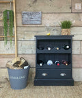 Dixie Belle Paint Midnight Sky Chalk Mineral Paint is the perfect paint for any DIY project! Black chalk painted wine cabinet with wine bottles inside and wine glasses, Also staged with a bucket of wood next to it.