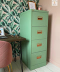 Dixie Belle Paint Mint Julep Chalk Mineral Paint is the perfect paint for any DIY project!
Mint green Chalk painted file cabinet. Staged in front of a tropical leaves wallpaper with a pink chair and wood desk with computer next to it.