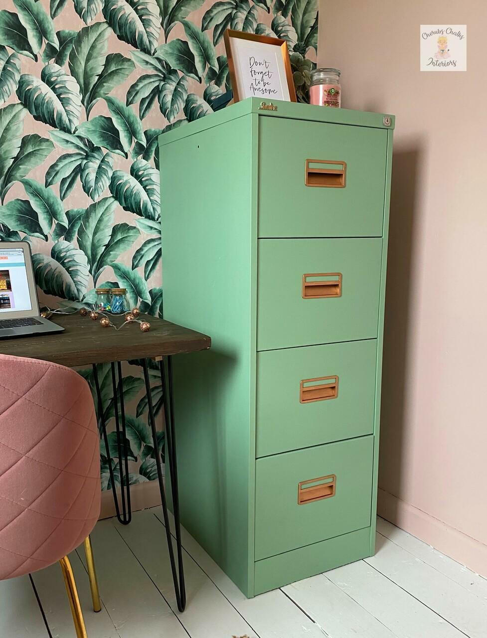 Dixie Belle Paint Mint Julep Chalk Mineral Paint is the perfect paint for any DIY project!
Mint green Chalk painted file cabinet. Staged in front of a tropical leaves wallpaper with a pink chair and wood desk with computer next to it.