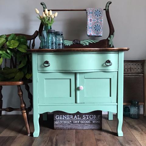 Dixie Belle Paint Mint Julep Chalk Mineral Paint is the perfect paint for any DIY project! Mint green Chalk Mineral painted washstand with a white knob and dark hard ware, and a dark wood stained  top with. Staged with three glass mason Jars and white tulips inside, and a pretty colorful towel on the rack.