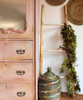 Moonshine metallic is the perfect paint to add shimmer and shine to your chalk painted furniture.  Armoire painted in pink moonshine metallic chalk mineral paint. Staged next to a blanket ladder, a wicker basket and greenery.