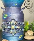 Moonshine metallic is the perfect paint to add shimmer and shine to your chalk painted furniture. Blue and purple moonshine metallic chalk mineral painted paint can with lotus rub on transfer and a wooden applique. Staged next to rocks.