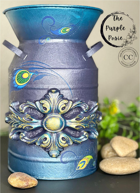Moonshine metallic is the perfect paint to add shimmer and shine to your chalk painted furniture. Blue and purple moonshine metallic chalk mineral painted paint can with lotus rub on transfer and a wooden applique. Staged next to rocks.