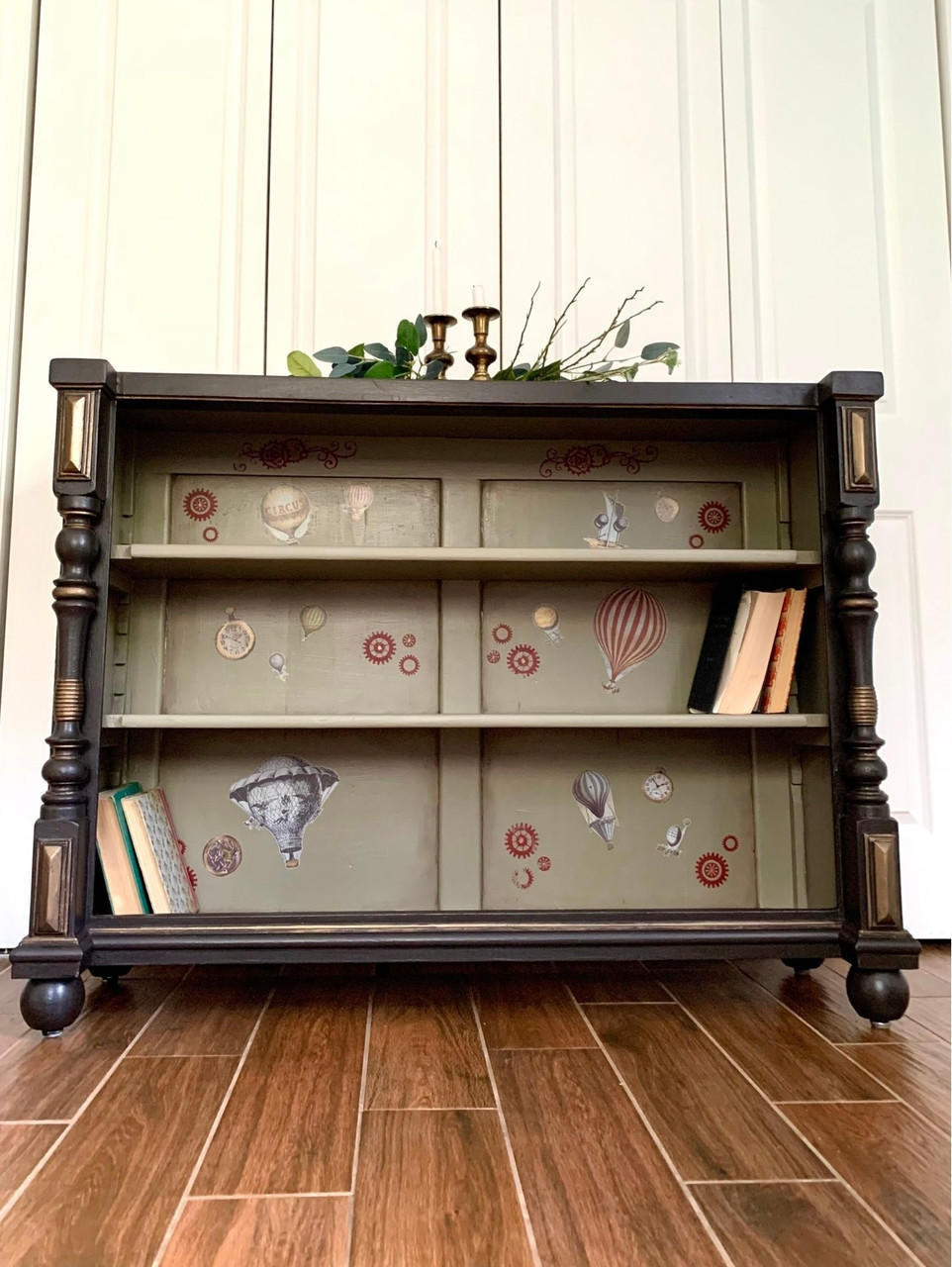 Dixie Belle Paint Mud Puddle Chalk Mineral Paint is the perfect paint for any DIY project! Bookcase painted black and blended with Dixie Belle Paint Mud Puddle Chalk Mineral Paint. Has air balloon rub on transfers inside. Staged with books and candles.