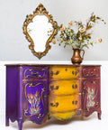 Dixie Belle Paint Muscadine Wine Chalk Mineral Paint is the perfect paint for any DIY project! Purple yellow and dark red chalk painted dresser with wheat style plants painted on. Staged with mirror and cheetah printed vase with roses.