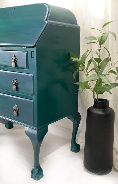 Dixie Belle Paint Palmetto Chalk Mineral Paint is the perfect paint for any DIY project! Up-close side view of a Green chalk painted secretary desk with gold hardware. Staged next to a black vase with a plant inside.