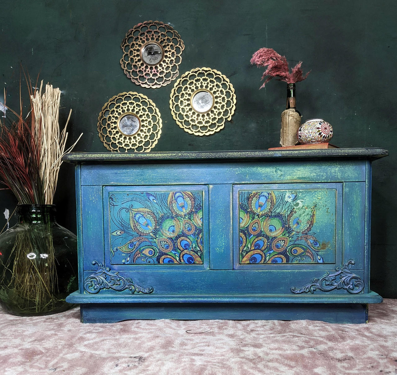 Dixie Belle Paint Peacock Chalk Mineral Paint is the perfect paint for any DIY project! Blue chalk painted blanket box with peacock rub on transfers and scroll wood applique. Staged with glass vase and plants inside.