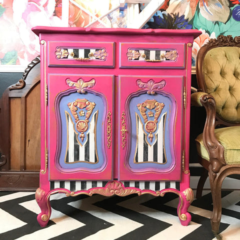 Dixie Belle Paint Peony Chalk Mineral Paint is the perfect paint for any DIY project! Pink chalk painted end table with black and white stripes on the front and light purple painted on the doors.