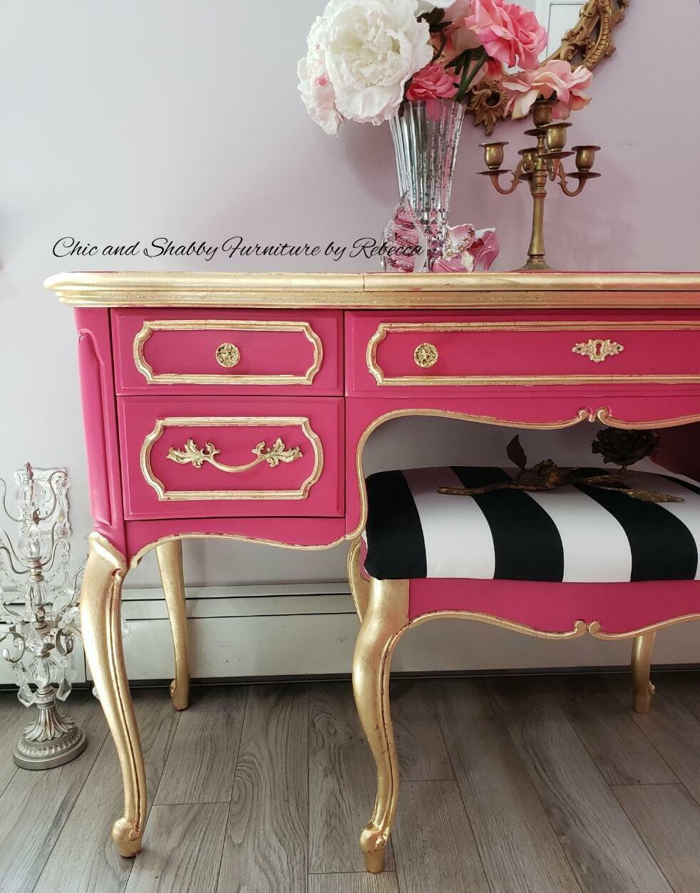Dixie Belle Paint Peony Chalk Mineral Paint is the perfect paint for any DIY project! Pink chalk painted desk  and chair with gold on the top, legs and on the scrolls. chair has black and white fabric. Staged next to a chandelier  and roses in a glass vase with a gold candle stick holder.