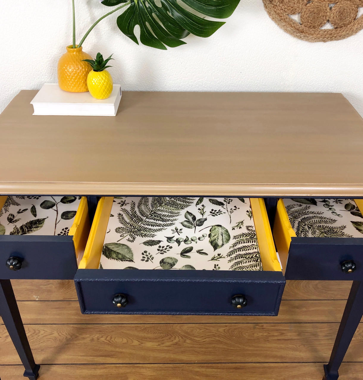 Dixie Belle Paint Pine Cone Chalk Mineral Paint is the perfect paint for any DIY project!  Chalk mineral painted desk with a light brown chalk paint on the top and dark blue for the body. With a tropical leaves print in the drawers. Staged with pineapples and plants.