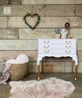 Dixie Belle Paint Pink Champagne Chalk Mineral Paint is the perfect paint for any DIY project! Light Pink chalk painted dresser with gold feet and gold hardware staged with a pink rug, wicker basket with blanket and pillow and plants and angel statue and lamp top.