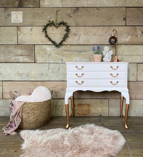 Dixie Belle Paint Pink Champagne Chalk Mineral Paint is the perfect paint for any DIY project! Light Pink chalk painted dresser with gold feet and gold hardware staged with a pink rug, wicker basket with blanket and pillow and plants and angel statue and lamp top.