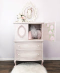 Dixie Belle Paint Pink Champagne Chalk Mineral Paint is the perfect paint for any DIY project! Light pink chalk painted armoire with a white blend and roses painted on the inside of the doors. Staged with little girl clothes and toys.