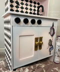 Dixie Belle Paint Pink Champagne Chalk Mineral Paint is the perfect paint for any DIY project! Kids play sink with a light pink and blue blend on the doors and black squares painted on the side and top cabinets. Alice rub on transfer on the door and the package staged next to it.