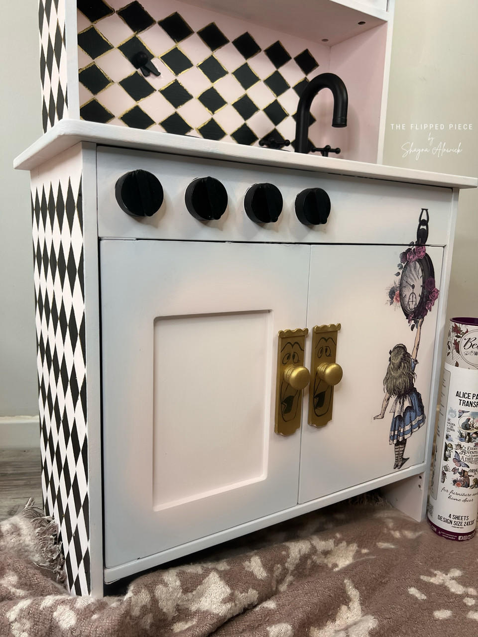 Dixie Belle Paint Pink Champagne Chalk Mineral Paint is the perfect paint for any DIY project! Kids play sink with a light pink and blue blend on the doors and black squares painted on the side and top cabinets. Alice rub on transfer on the door and the package staged next to it.