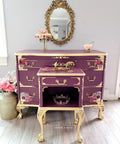 Dixie Belle Paint Plum Crazy Chalk Mineral Paint is the perfect paint for any DIY project! Dresser and end table painted in a maroon chalk paint with gold feet, gold hardware and gold trim. Staged with pink flowers, a tiara and a gold mirror.