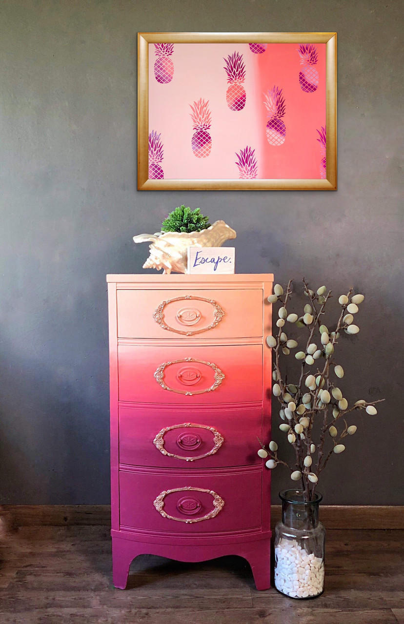 Dixie Belle Paint Plum Crazy Chalk Mineral Paint is the perfect paint for any DIY project! End table chalk painted in maroon, coral and apricot blended together with gold on the trims in the front. Staged with a conch shell with a plant, a pineapple picture and glass vase with a plant inside.