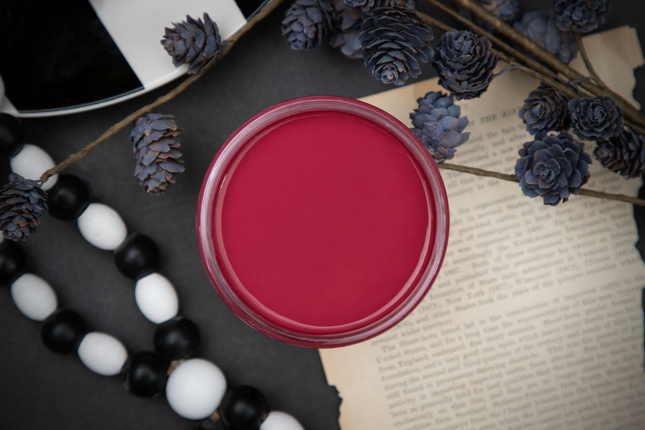Dixie Belle Paint Plum Crazy Chalk Mineral Paint is the perfect paint for any DIY project! Open top view of a maroon chalk paint. Staged with black and white wood beads and black floral plants.