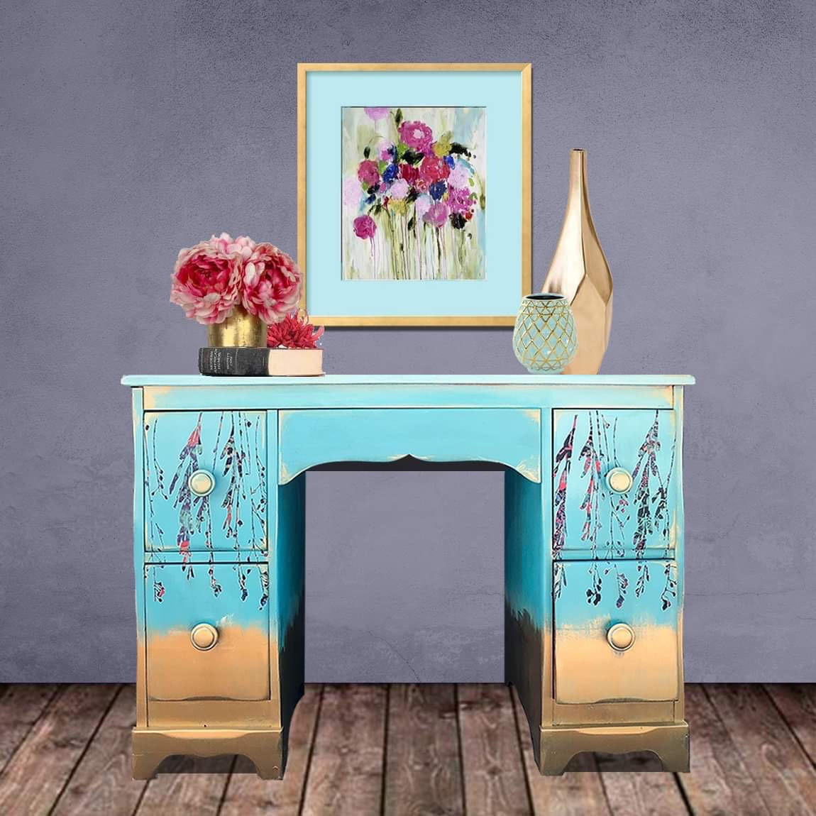 Dixie Belle Paint Pure Ocean Chalk Mineral Paint is the perfect paint for any DIY project! Blue chalk painted desk with gold ends and hardware and floral rub on transfers. Staged with pink plants and gold vases.