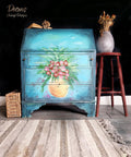 Dixie Belle Paint Pure Ocean Chalk Mineral Paint is the perfect paint for any DIY project! dark blue to light blue Ombre chalk painted secretary cabinet with hand painted flowers in a vase. Staged with potted plants and wicker basket.
