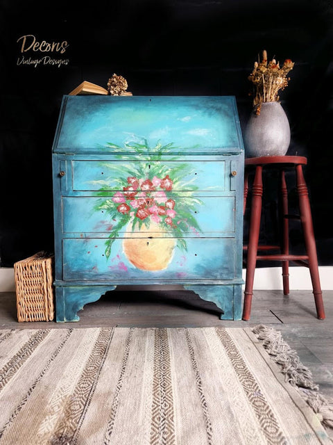 Dixie Belle Paint Pure Ocean Chalk Mineral Paint is the perfect paint for any DIY project! dark blue to light blue Ombre chalk painted secretary cabinet with hand painted flowers in a vase. Staged with potted plants and wicker basket.