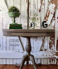 Dixie Belle Paint Putty Chalk Mineral Paint is the perfect paint for any DIY project! A muted taupe colored table staged in front of a rustic door with various green props on top such as books, plant with a plant stand and the letter G.