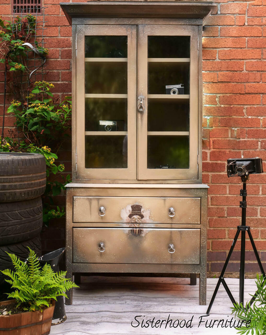 Dixie Belle Paint Putty Chalk Mineral Paint is the perfect paint for any DIY project! An armoire cabinet painted in a muted taupe with various brown tones and a steampunk transfer on the front staged in front of a brick building with greenery surrounding.