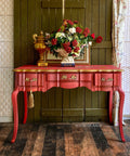 Dixie Belle Paint Rustic Red Chalk Mineral Paint is the perfect paint for any DIY project! A vintage table featuring the rustic red and the sides and hardware are accentuated with gold. This table has a gloss sheen and is staged with flowers and books on top.