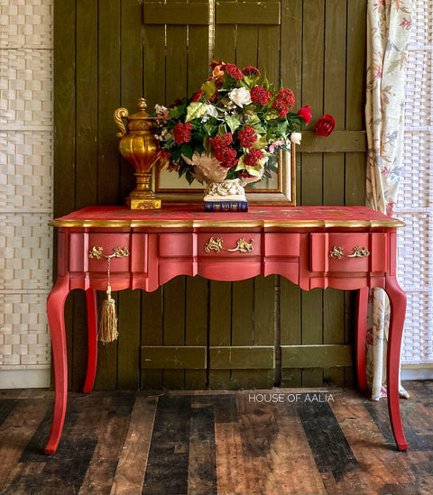 Dixie Belle Paint Rustic Red Chalk Mineral Paint is the perfect paint for any DIY project! A vintage table featuring the rustic red and the sides and hardware are accentuated with gold. This table has a gloss sheen and is staged with flowers and books on top.