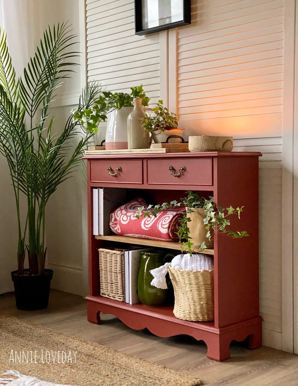 Dixie Belle Paint Rusty Nail Chalk Mineral Paint is the perfect paint for any DIY project! An entertainment bookshelf painted in the rusty nail with various items on the 2 bottom shelves and 2 drawers on top. This bookshelf is staged with greenery.