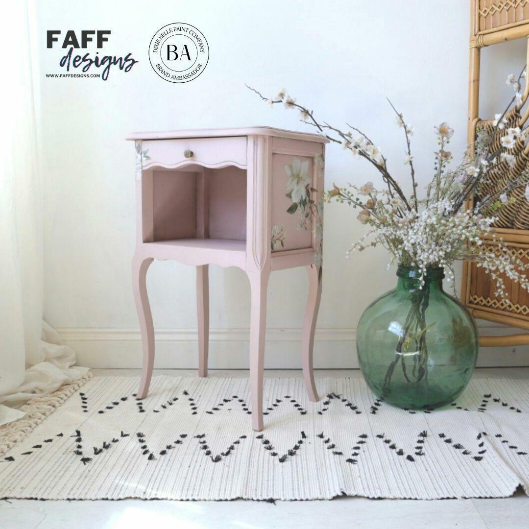 Dixie Belle Paint Tea Rose Chalk Mineral Paint is the perfect paint for any DIY project!
Bedside table painted in Tea Rose Chalk Mineral Paint  with the Magnolia Garden  Transfer on the side panels. Staged on a boho light tan rug and a large green round glass flower vase.