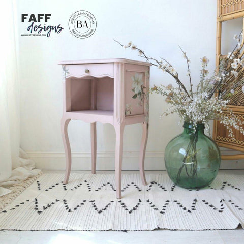 Dixie Belle Paint Tea Rose Chalk Mineral Paint is the perfect paint for any DIY project!
Bedside table painted in Tea Rose Chalk Mineral Paint  with the Magnolia Garden  Transfer on the side panels. Staged on a boho light tan rug and a large green round glass flower vase.