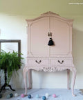 Dixie Belle Paint Tea Rose Chalk Mineral Paint is the perfect paint for any DIY project!
A large drink cabinet painted in Tea Rose Chalk Mineral Paint with dark hardware and a black tassle on the door handle. Staged on top of a white fringe rug, party lights on the floor and greenery.