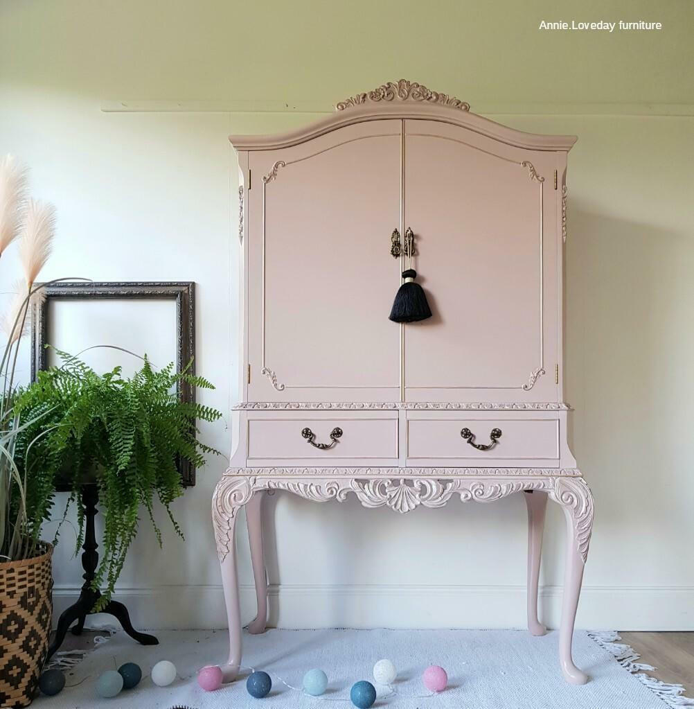 Dixie Belle Paint Tea Rose Chalk Mineral Paint is the perfect paint for any DIY project!
A large drink cabinet painted in Tea Rose Chalk Mineral Paint with dark hardware and a black tassle on the door handle. Staged on top of a white fringe rug, party lights on the floor and greenery.