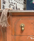 Dixie Belle Paint Terracotta Chalk Mineral Paint is the perfect paint for any DIY project!  A closeup picture of the front of a brown chalk painted dresser with a gold pull knob and a tassel hanging off of it.