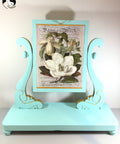 Dixie Belle Paint The Gulf Chalk Mineral Paint is the perfect paint for any DIY project!  A blue chalk painted picture stand holding a printed picture of a white flower.