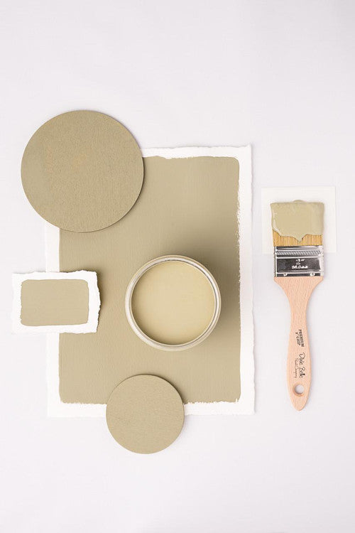 A paintbrush with green paint lies next to a jar filled with the same color. Green paint swatches and round samples are arranged around the jar on a light background.