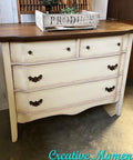 Dixie Belle Paint Drop Cloth Chalk Mineral Paint is the perfect paint for any DIY project! A vintage-style dresser with a dark wooden top and distressed cream-colored body featuring two small upper drawers and two large lower drawers. A wooden crate marked "Produce" and a small plant sit on top. Text reads "Creative Moments.