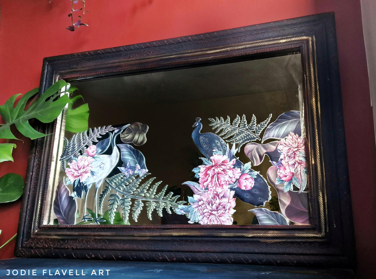 Elegant Avian Flora Transfer applied on a mirror. Mirror frame is painted with a dark purplish black. Staged against a red wall.