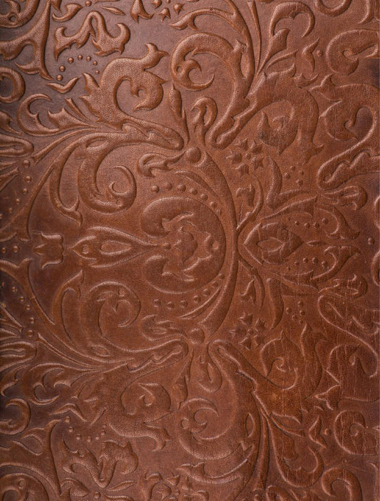 Close-up of a brown leather surface with intricate embossed floral patterns. The design includes swirling leaves and blooms, creating a textured, elegant appearance.